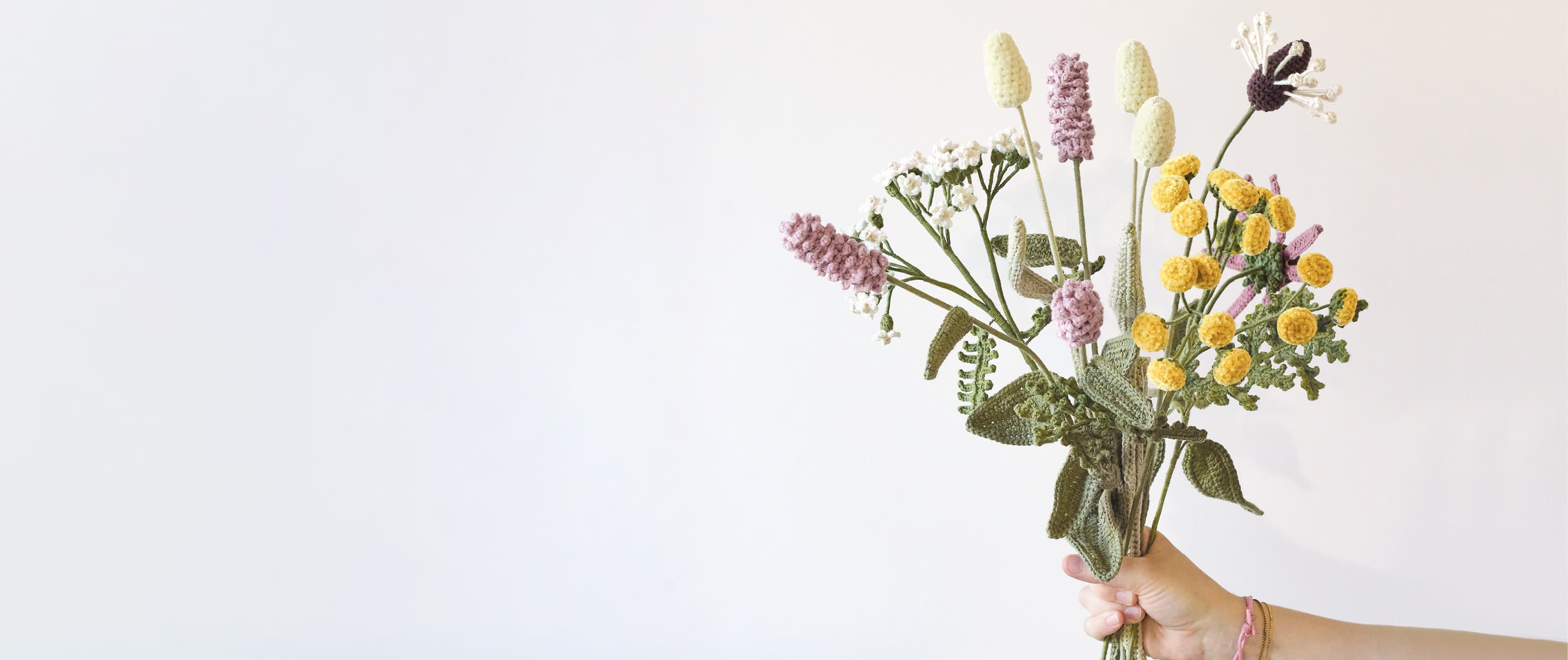 Eine Hand hält gehäkelte Wildblumen, die zu einem Blumenstrauß arrangiert sind.