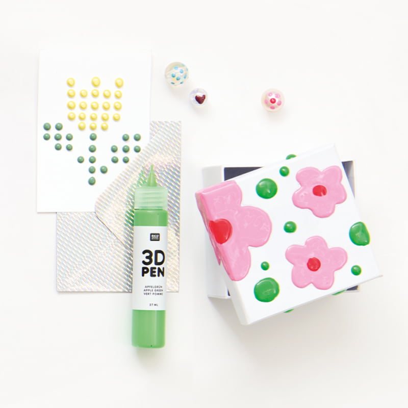 Bemalte Karte und Schachtel mit 3D Effekten liegen zusammen mit einem 3D Pen auf grauem Hintergrund.