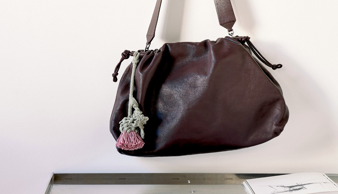Material Ricorumi In the Meadow Taschenanhänger an großer Schultertasche, gehäkelter Anhänger mit Blüte aus Garn, dekorativ präsentiert an heller Wand
