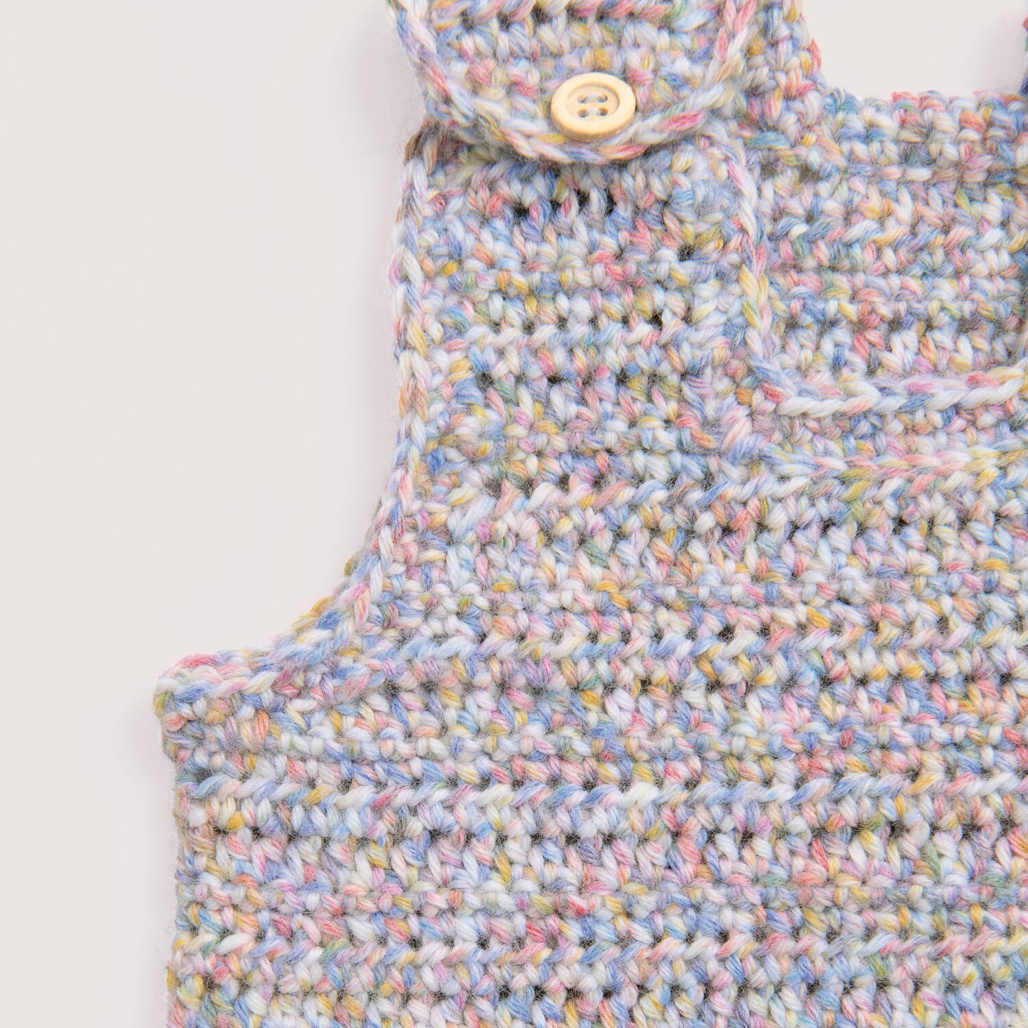 Rico Baby Dream dk A Luxury Touch zeigt eine gehäkelte Baby-Latzhose aus vielseitig pastellfarbenem Rico Design Garn mit Holzknopf, ideal für weiche Kindermode