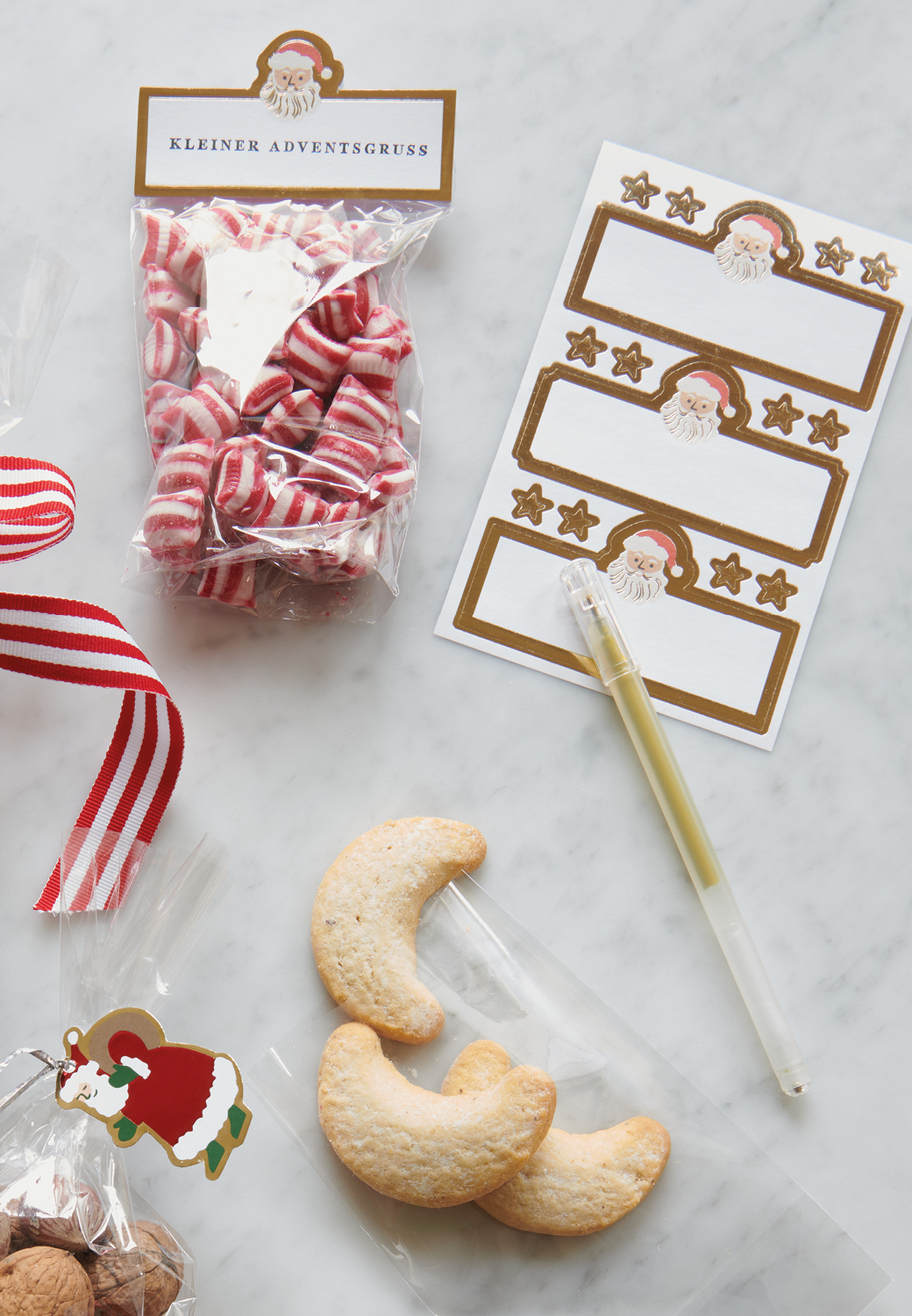 Gefüllte Tüten mit Bonbons und Vanillekipferln liegen mit Papieretiketten mit goldenem Rahmen auf Marmoruntergrund