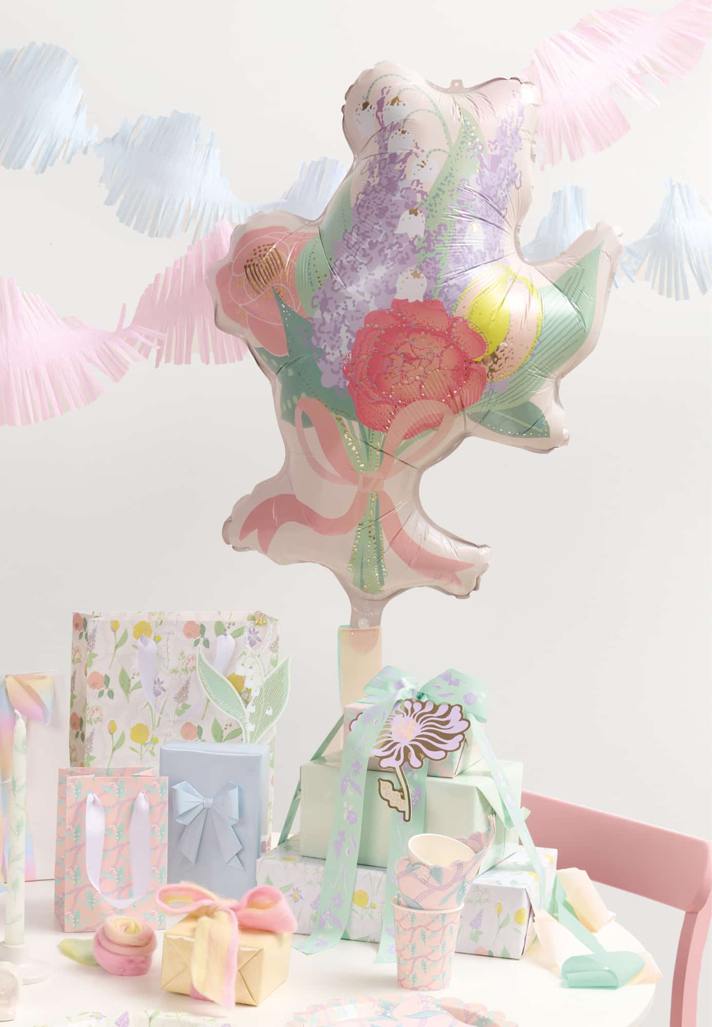 Ein Partytisch ist mit Geschenken, einem Blumenstrauß-Folienballon und Geschirrsets geschmückt.