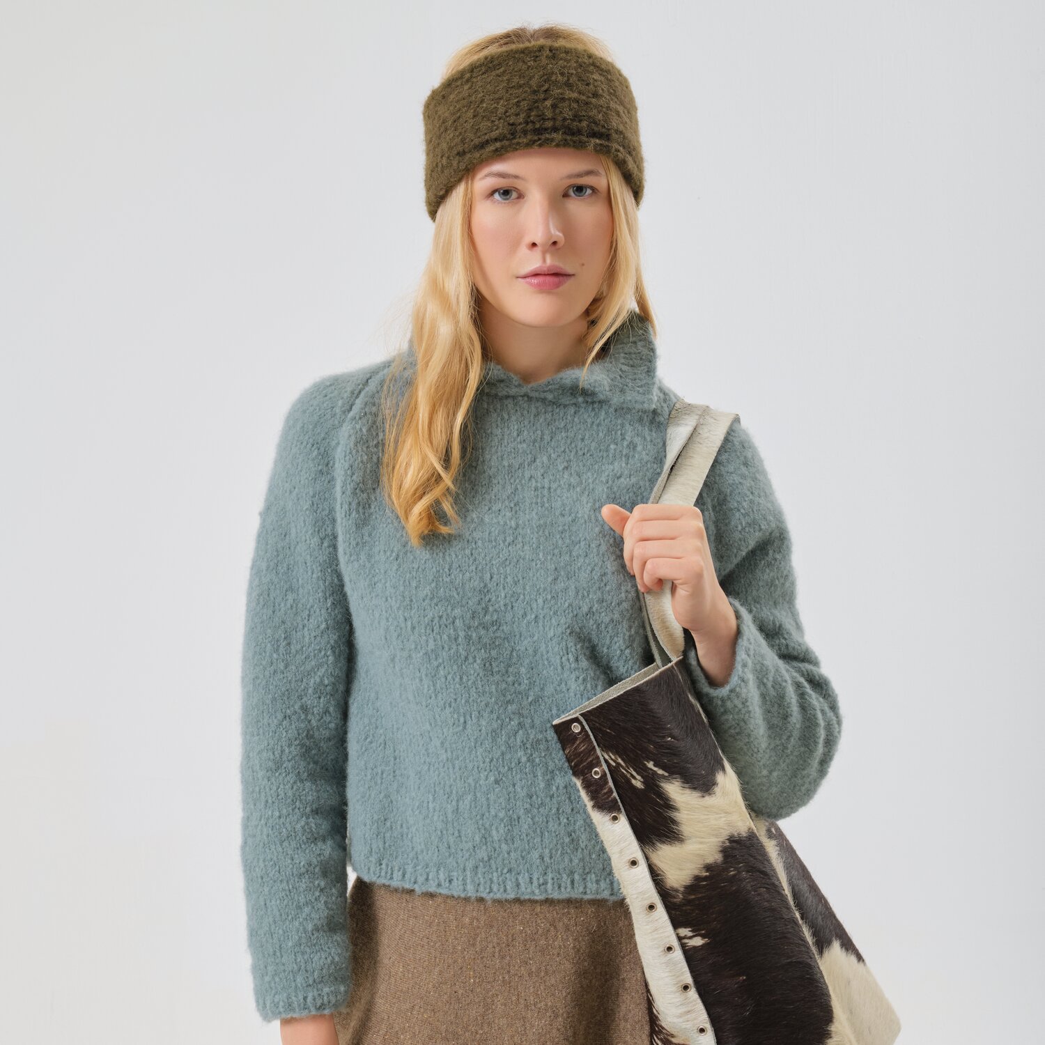 Strickset Pullover Modell 13a aus Made by Me No. 21 von Rico Design Strickset Pullover Modell 13a: Frau in blauem Pullover mit braunem Stirnband und gemusterter Tasche.