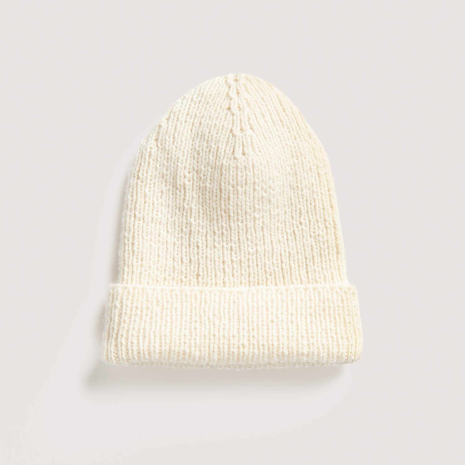 Luxury Knits - Premium Natural Fibres Sprachauswahl deutsch von Rico Design Strickset Mütze Modell 06 aus Luxury Knits: Cremefarbene, handgestrickte Mütze aus hochwertigen Naturfasern auf hellem Hintergrund.