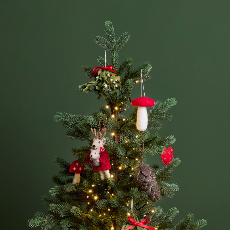 Ein geschmückter Weihnachtsbaum steht vor einer dunkelgrünen Wand. 