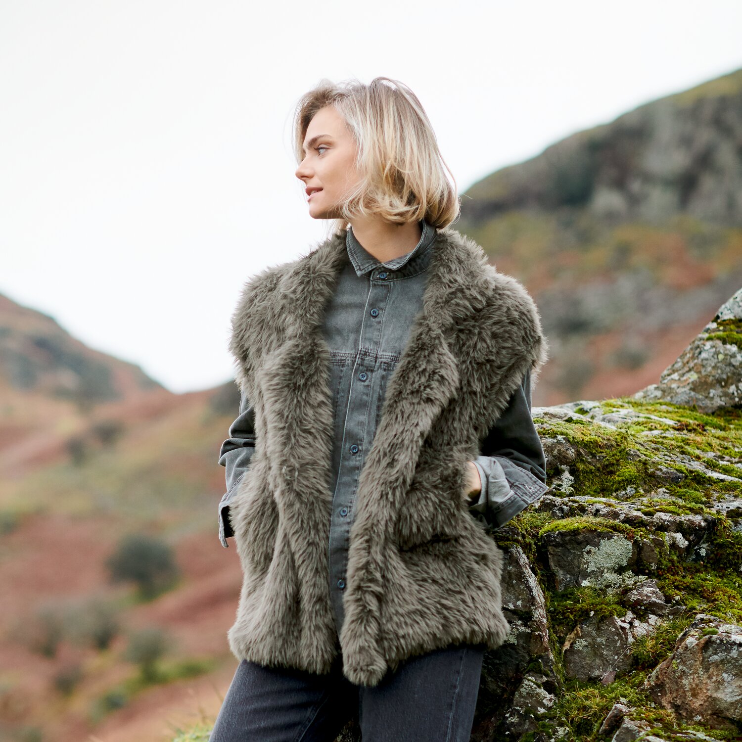 Strickset Weste Modell 14 aus Lovewool No. 23, flauschige ärmellose Strickweste in Naturton über Jeansjacke, getragen von Frau in herbstlicher Berglandschaft