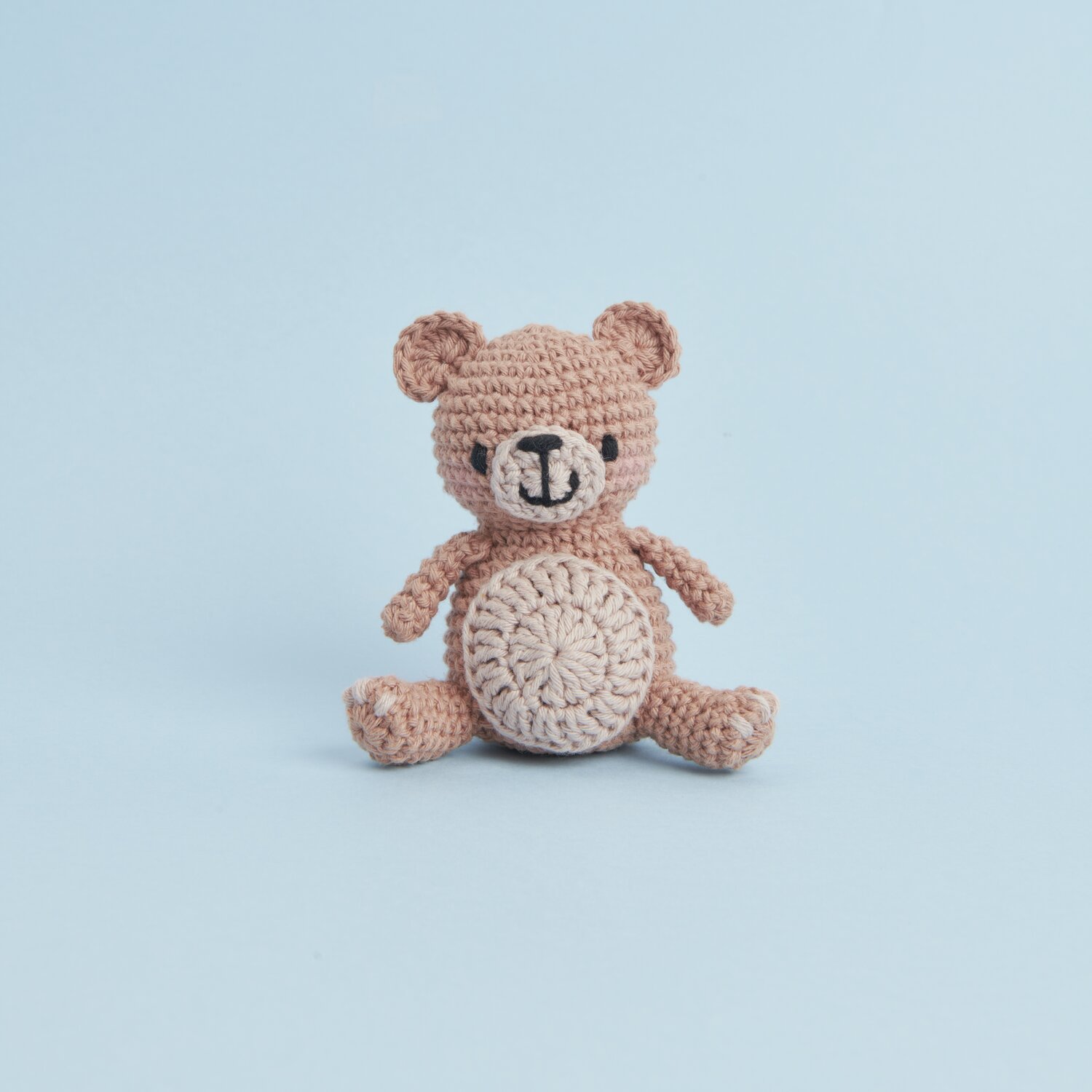 Ricorumi Mini Easy Häkelset - Teddy: Beigefarbener gehäkelter Teddybär von Rico Design vor blauem Hintergrund.