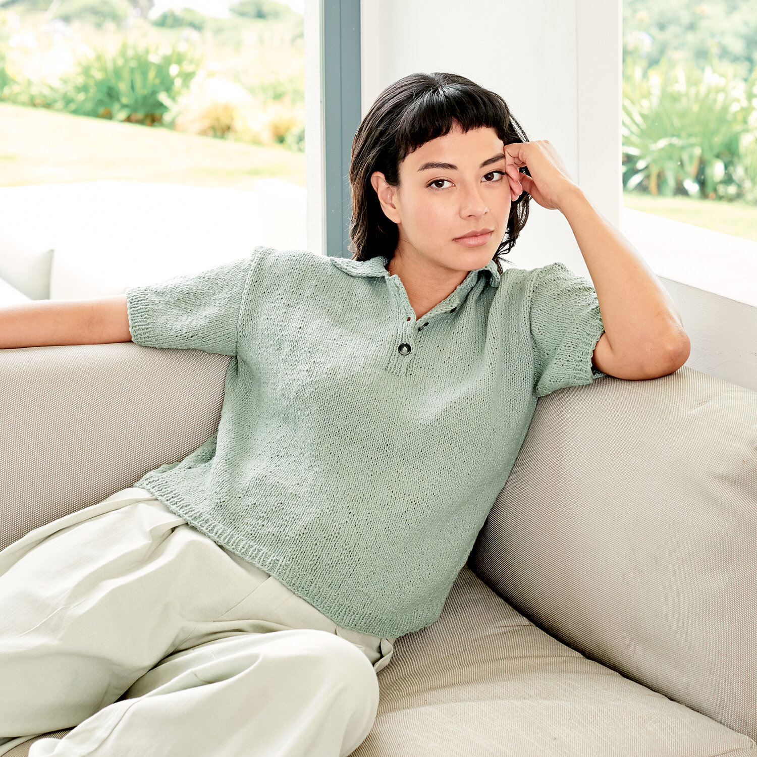 Strickanleitung Polo-Shirt aus Essentials Super Cotton dk, leger geschnittenes Poloshirt in sanftem Pastellton, glatt rechts gestrickt, kurze Ärmel, getragen von Person auf Sofa
