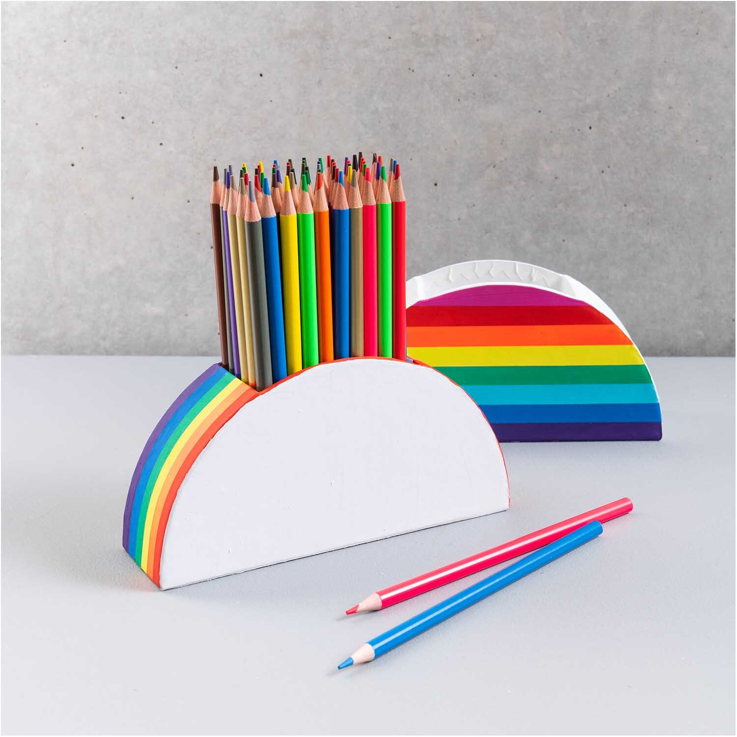 Stiftehalter aus Pappe halbrund mit Regenbogenmuster, gefüllt mit bunten Buntstiften, von Rico Design.