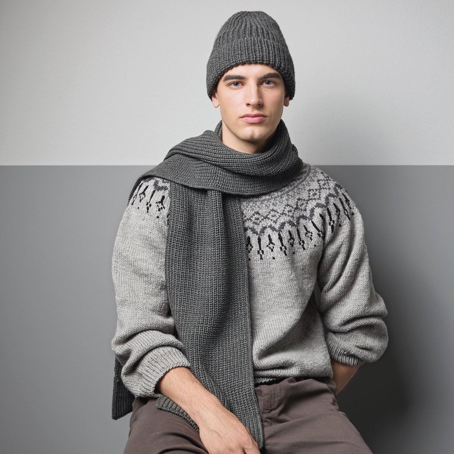 Strickset Mütze Modell 17 aus Made by Me Men No. 3 von Rico Design Strickset Mütze Modell 05 aus Made by Me Men No. 3: Mann trägt graue Mütze und Schal, kombiniert mit gestricktem Pullover in modernem Design.