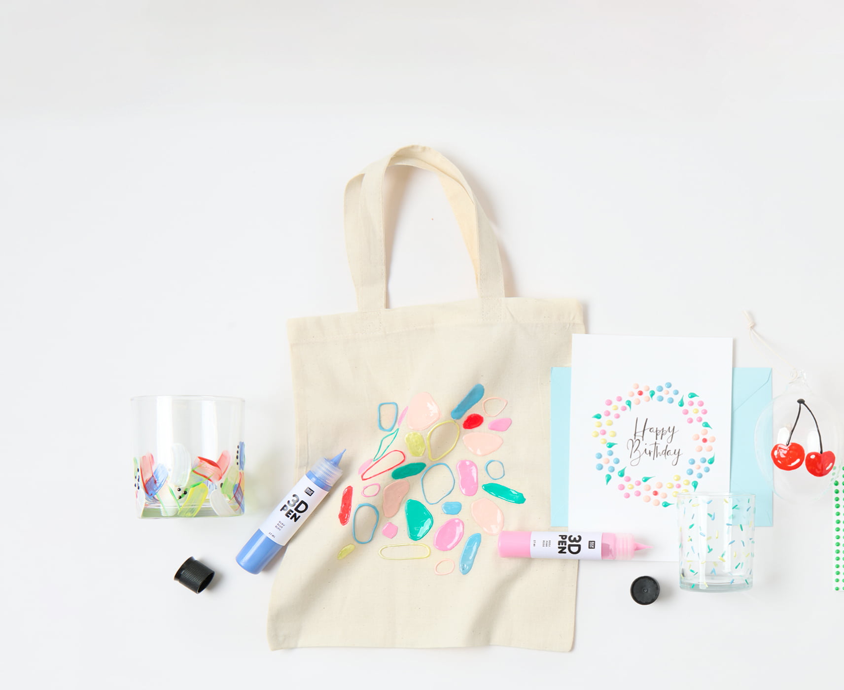 Bunt bemalte Karte, Taschen und Gläser mit 3D- und Perlen-Effekten, liegen umgeben von bunten 3D-Pens auf grauem Hintergrund.