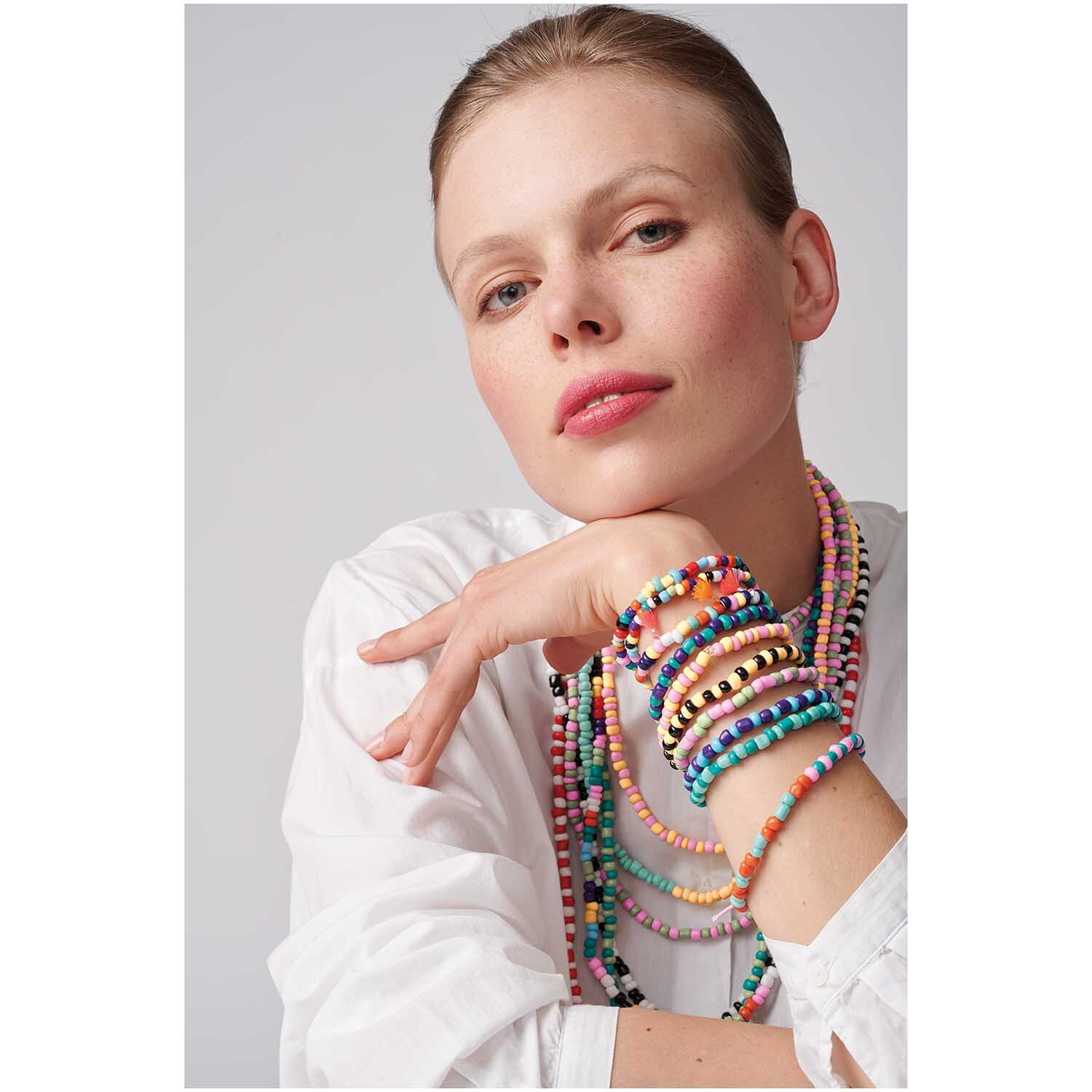 Keramik-Perlen natur multicolor 3mm 30g: Frau trägt bunte Halsketten und Armbänder aus Keramikperlen von Rico Design.