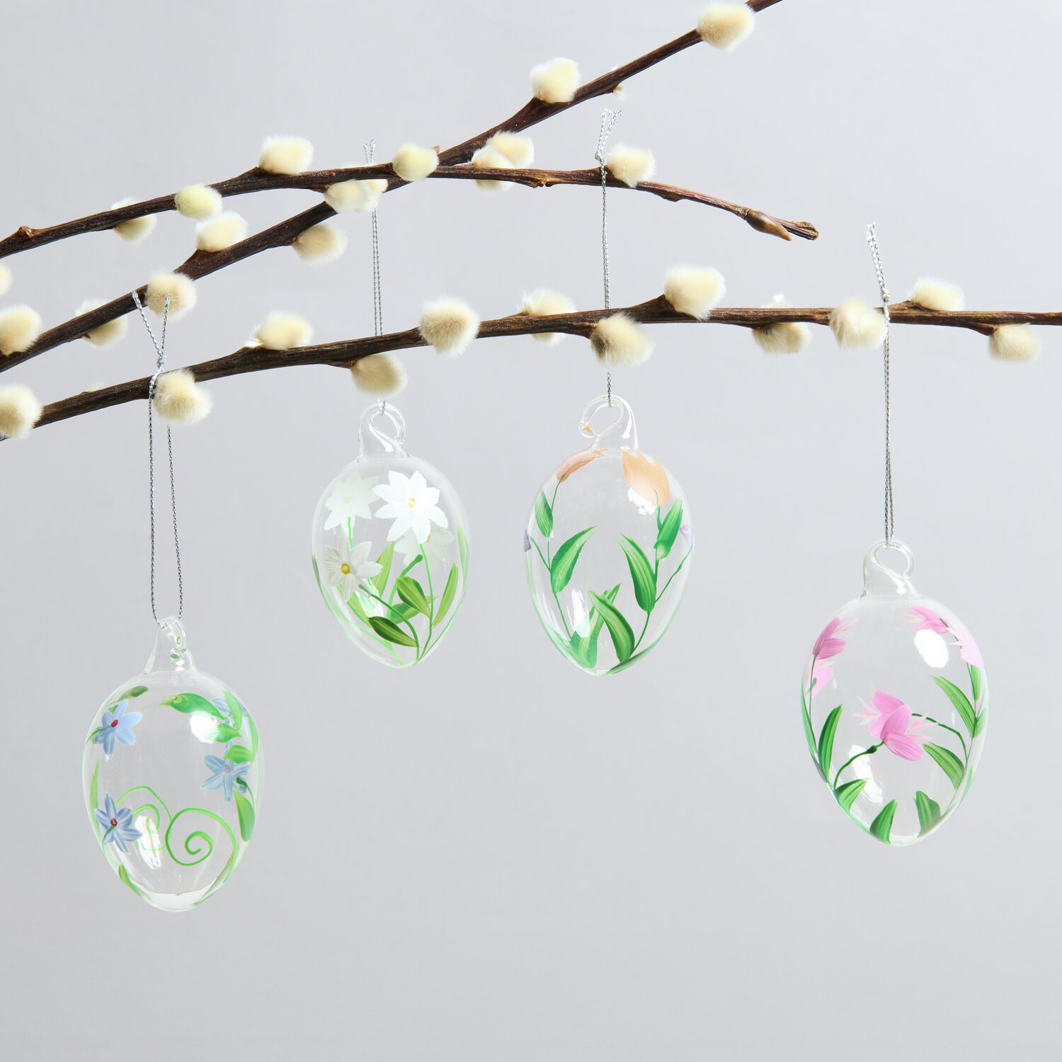 Glas Eier Blumenwiese handbemalt 4 Stück: Vier dekorative, handbemalte Glaseier mit Blumenmotiven hängen an einem Ast.