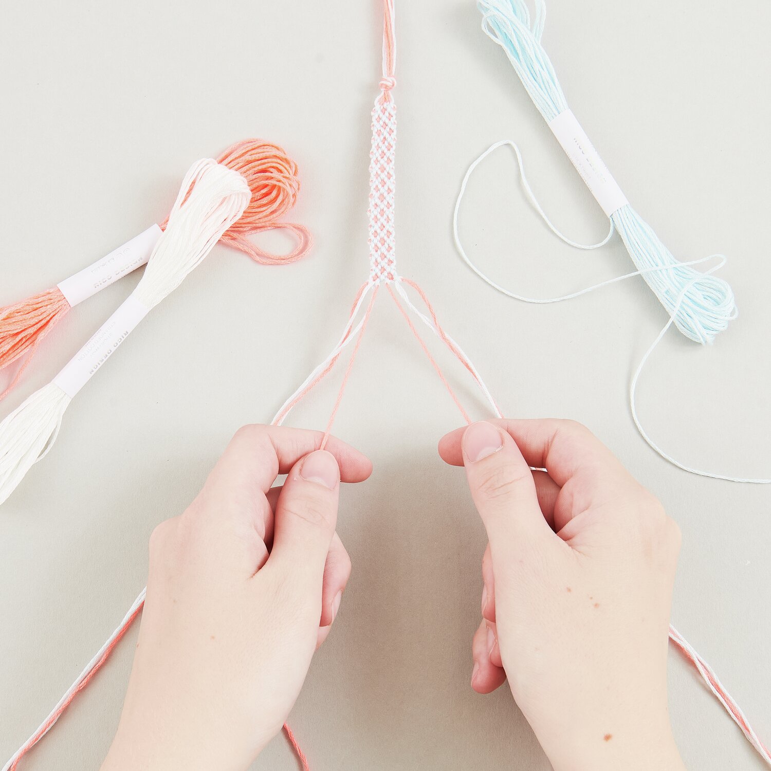 DIY Freundschaftsarmbänder Set Pastel Colours: Hände flechten bunte Fäden in Pastelltönen.