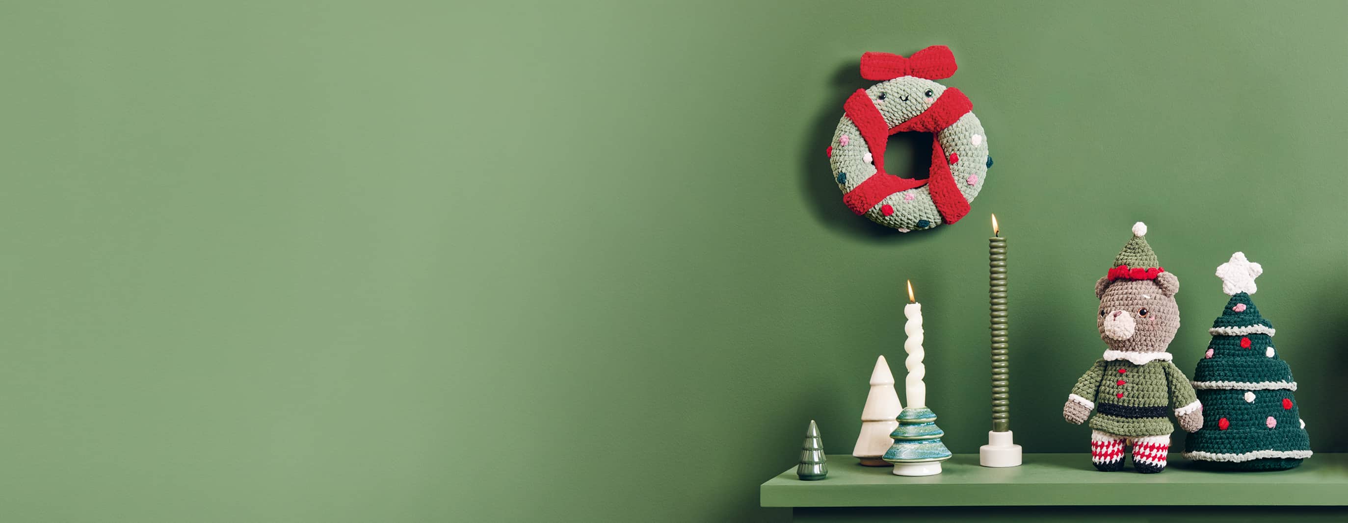 Weihnachtliche Häkelfiguren aus Chenille-Garn sind dekoriert auf einem Regal und an einer grünen Wand dekoriert