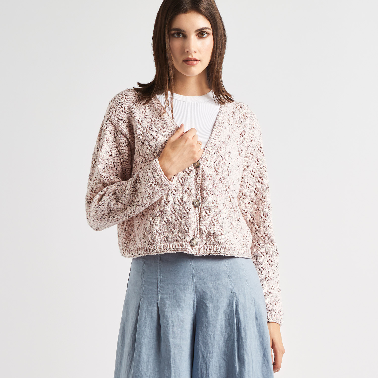 Strickanleitung Lochmusterjacke mit Beilaufgarn: Elegante, beige Jacke mit Lochmuster, kombiniert mit einem blauen Rock. Ideal für den Frühling.