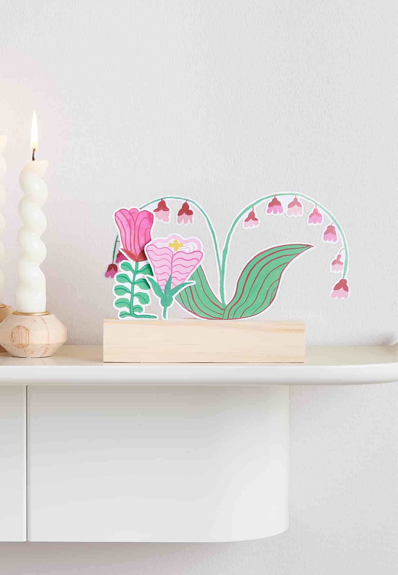 Dekoration aus Bastelpapier mit Blumenmotiv in einem Holzaufsteller auf einem Regal dekoriert