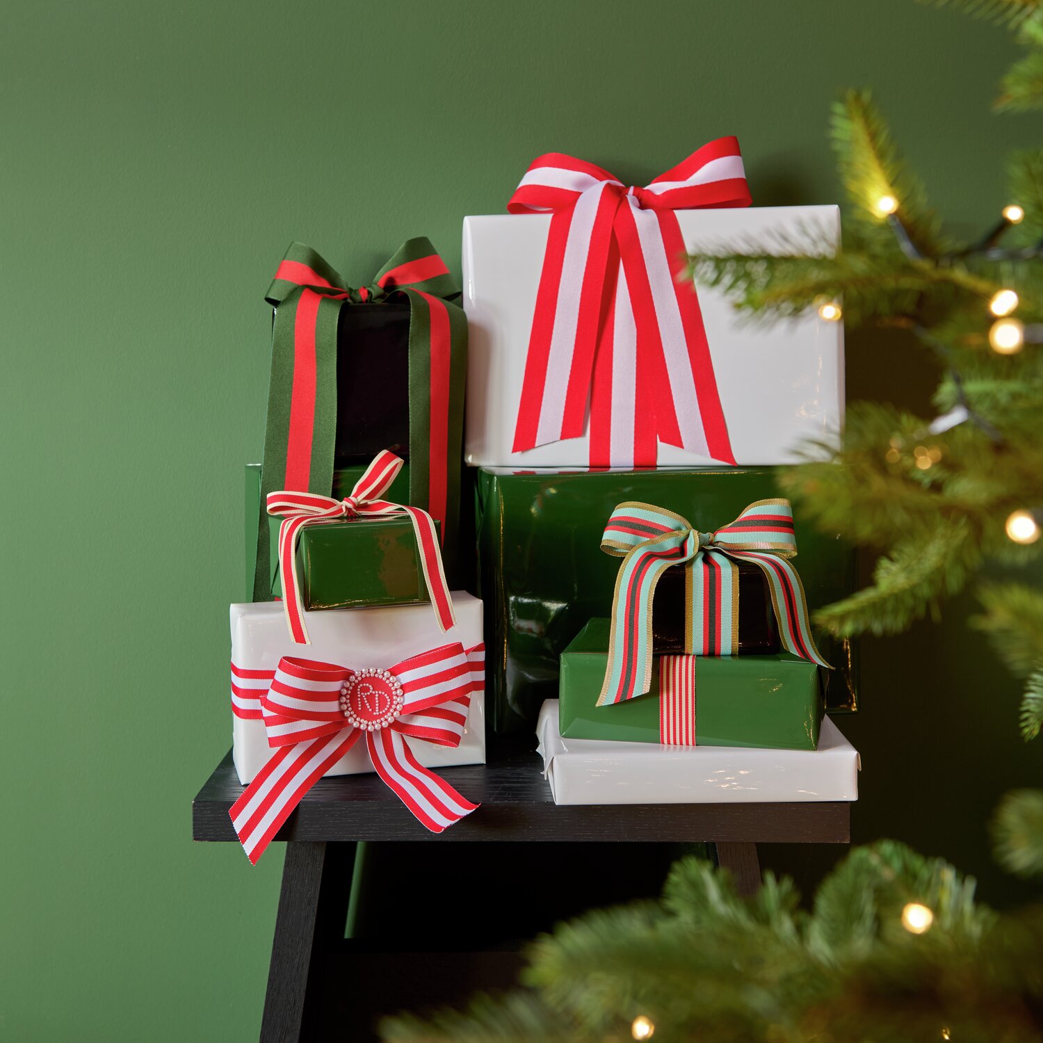 Geschenkverpackungen in Schwarz, Grün und Weiß von Rico Design, dekoriert mit roten und gestreiften Schleifen, auf einem Tisch vor einem grünen Hintergrund. Perfekt für festliche Anlässe.