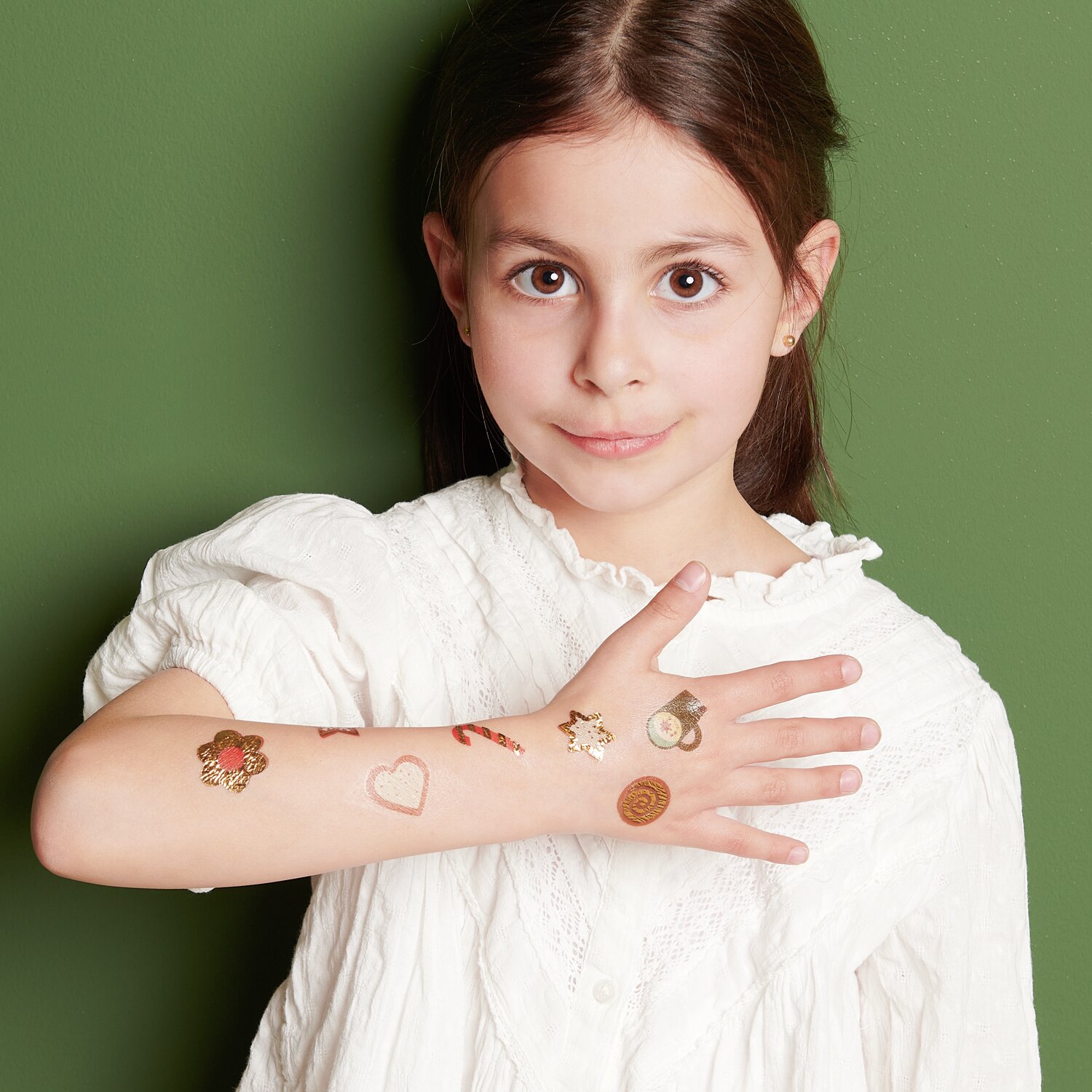 Tattoos Weihnachten: Mädchen mit festlichen Tattoos auf dem Arm, vor grünem Hintergrund.