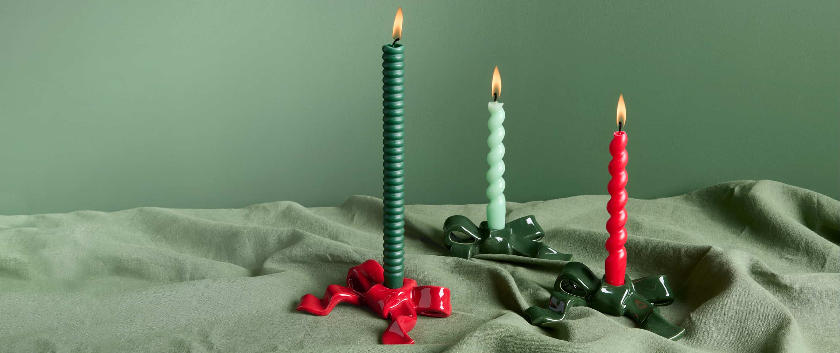 Kerzenhalter Schleife bestückt mit brennenden Kerzen stehen auf grünem Stoff.