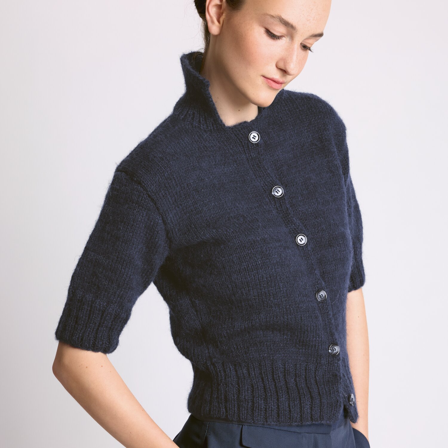 Strickset Jacke Modell 14 aus Luxury Knits - Premium Natural Fibres von Rico Design Strickset Jacke Modell 14 aus Luxury Knits: Dunkelblaue, kurzärmelige Strickjacke mit Knopfleiste, getragen von einer Frau.