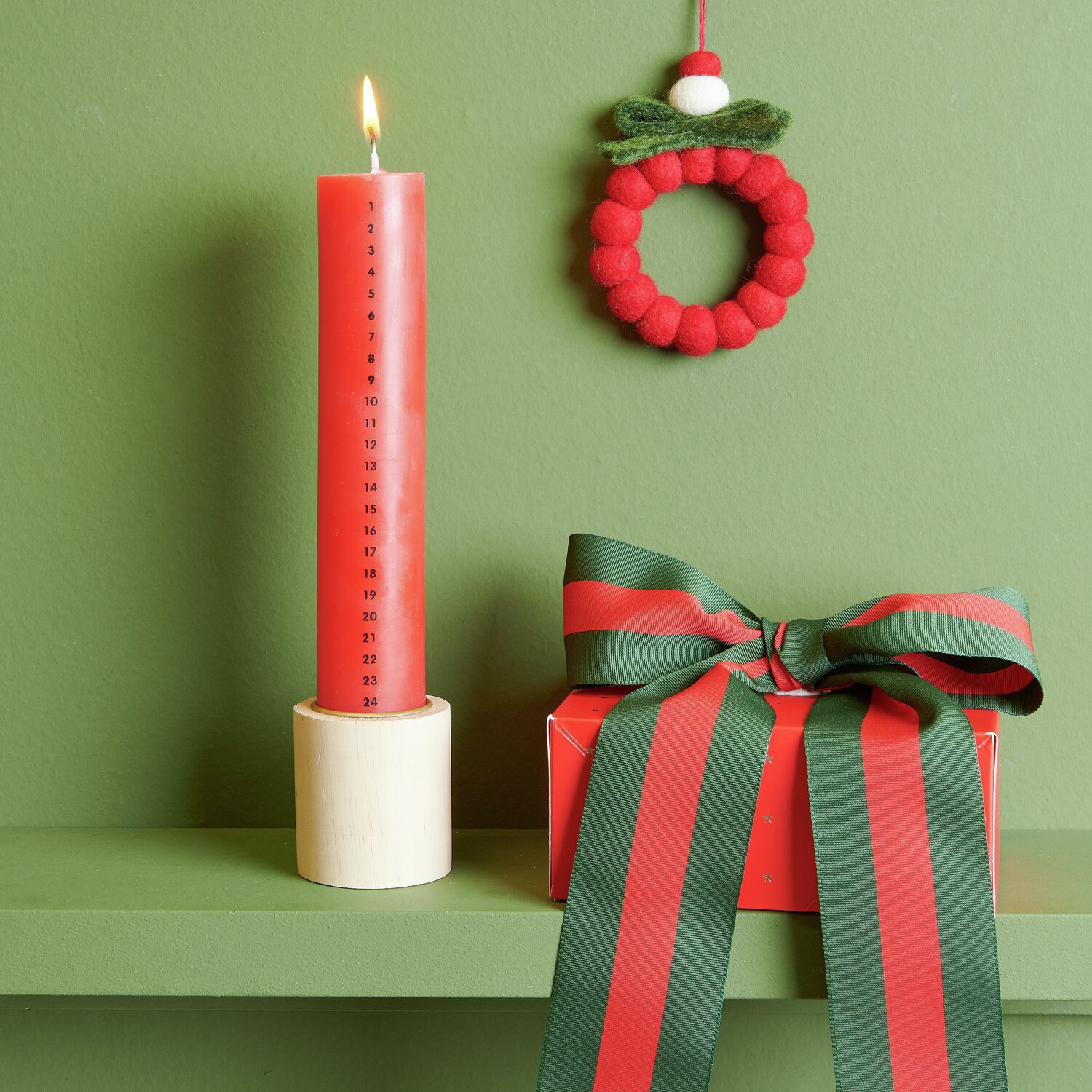 Adventskalender Kerze Ø4x20cm Farbe Rot von Rico Design Adventskalender Kerze, rot, Ø4x20cm, auf grünem Regal mit Geschenkbox und Dekokranz.