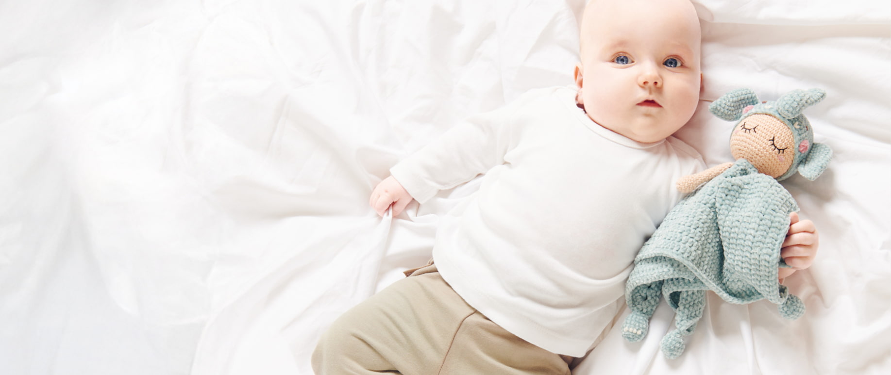 Baby liegt mit gehäkeltem Elefanten-Schmusetuch im Arm auf einer Decke