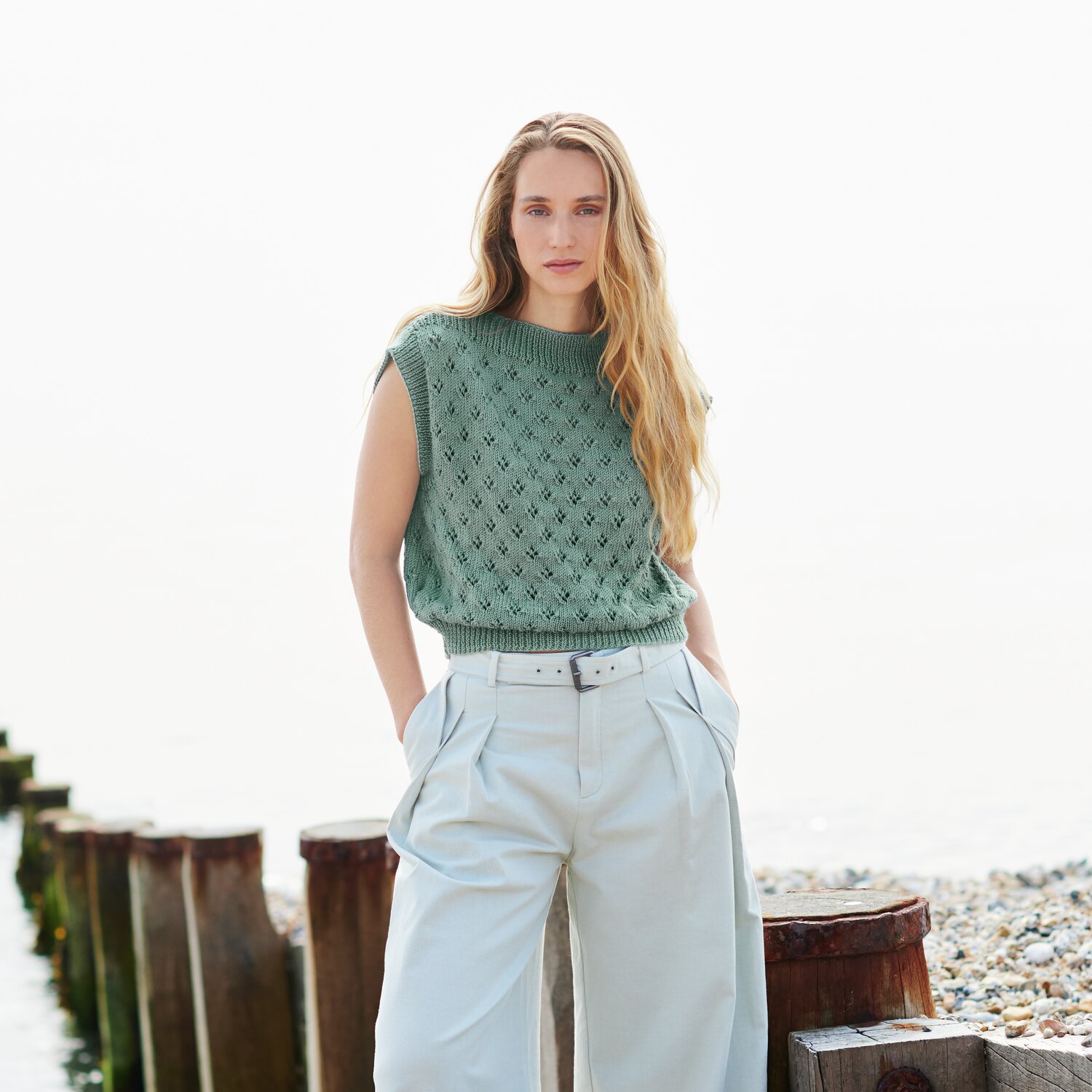 Strickset Top Modell 26 aus Lovewool No. 22: Frau in grünem Stricktop und hellen Hosen am Strand.