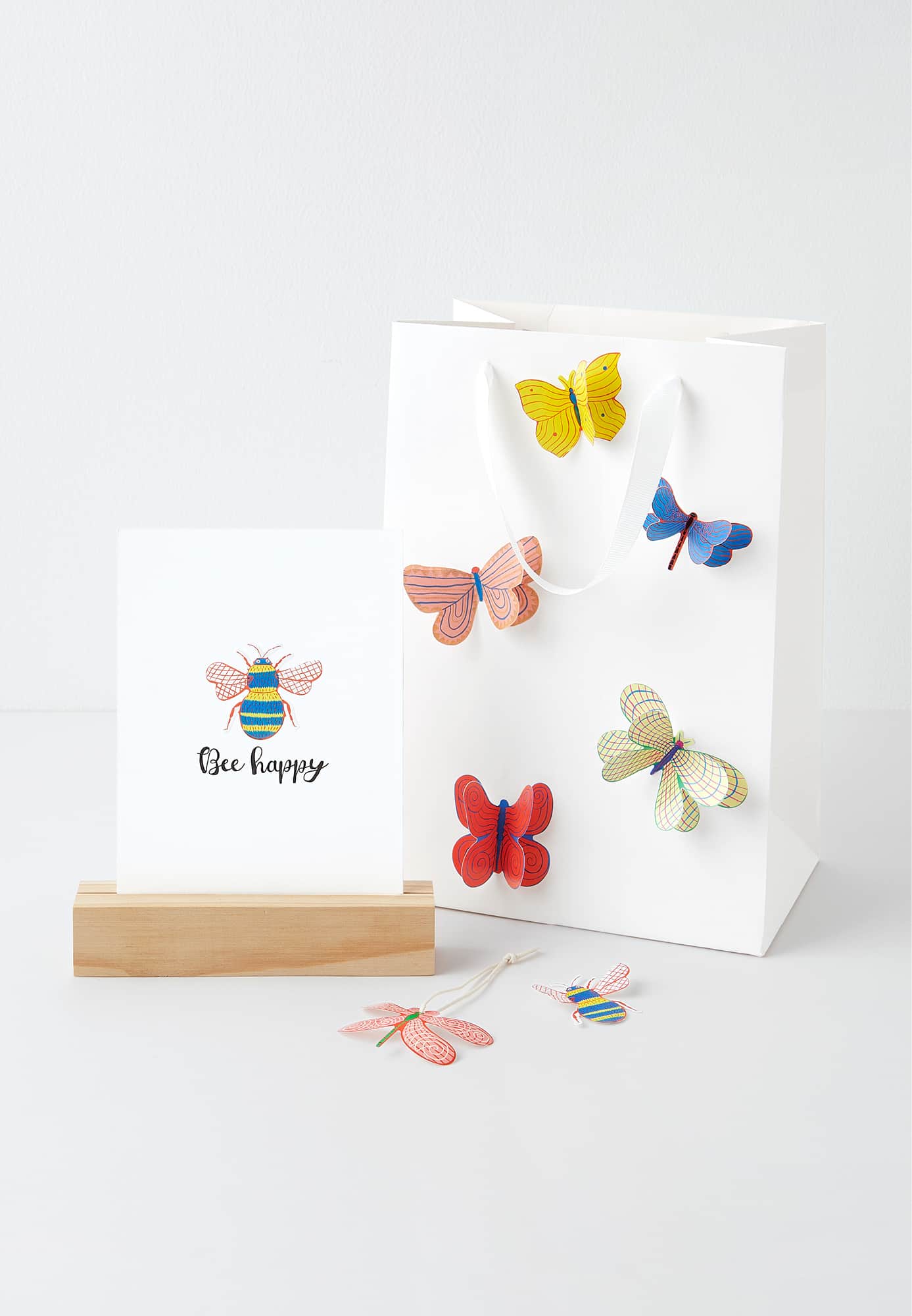 Karte in Holzaufsteller und weiße Papiertüte mit 3D Schmetterling-Stickern verziert 