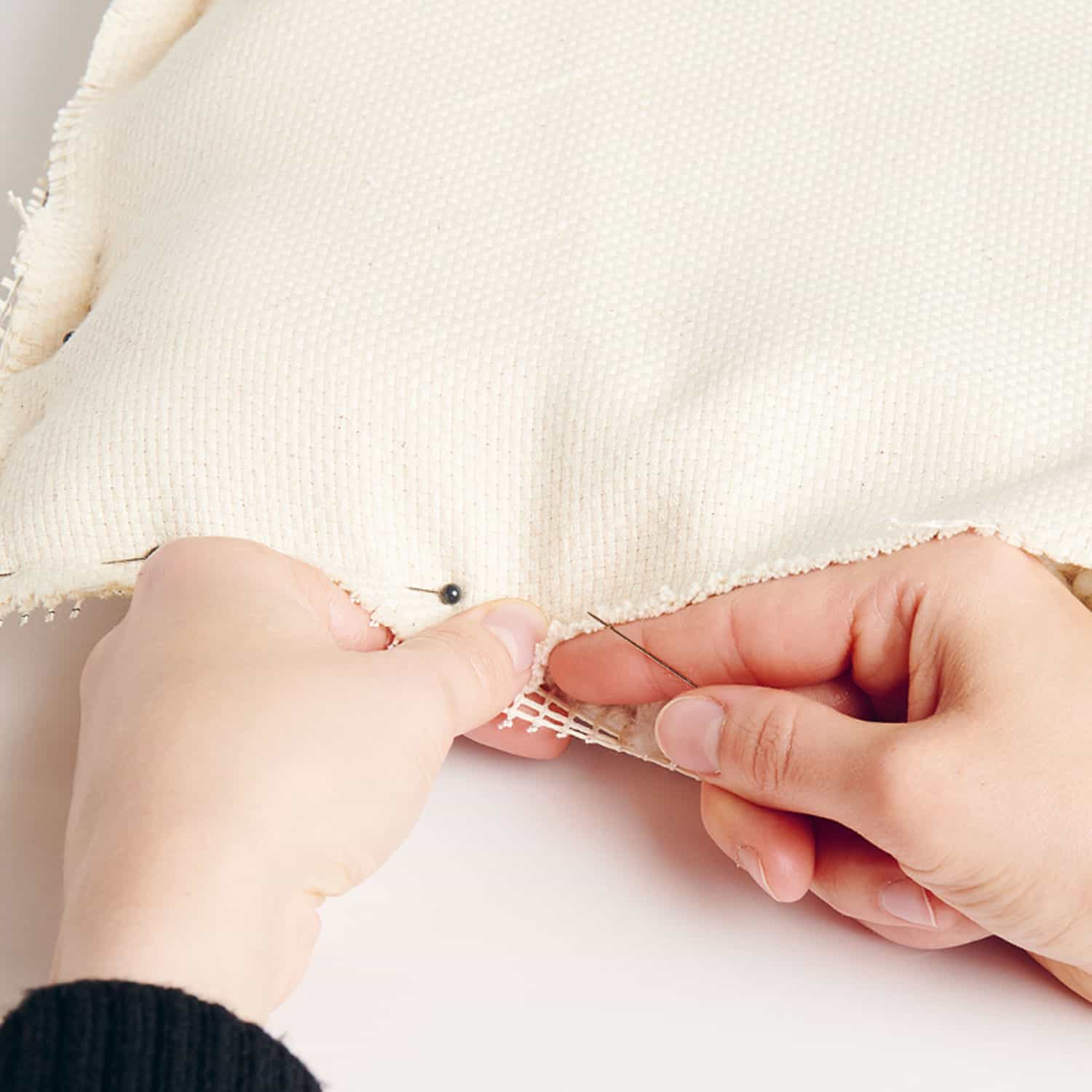 Hände stecken Stramin an einem Kissenbezug mit einer Nadel fest