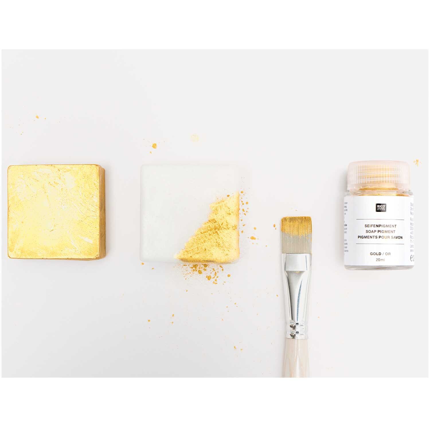 Seifenpigment gold 20ml: Goldene Pigmentflasche von Rico Design neben Pinsel und bemalter Seife.