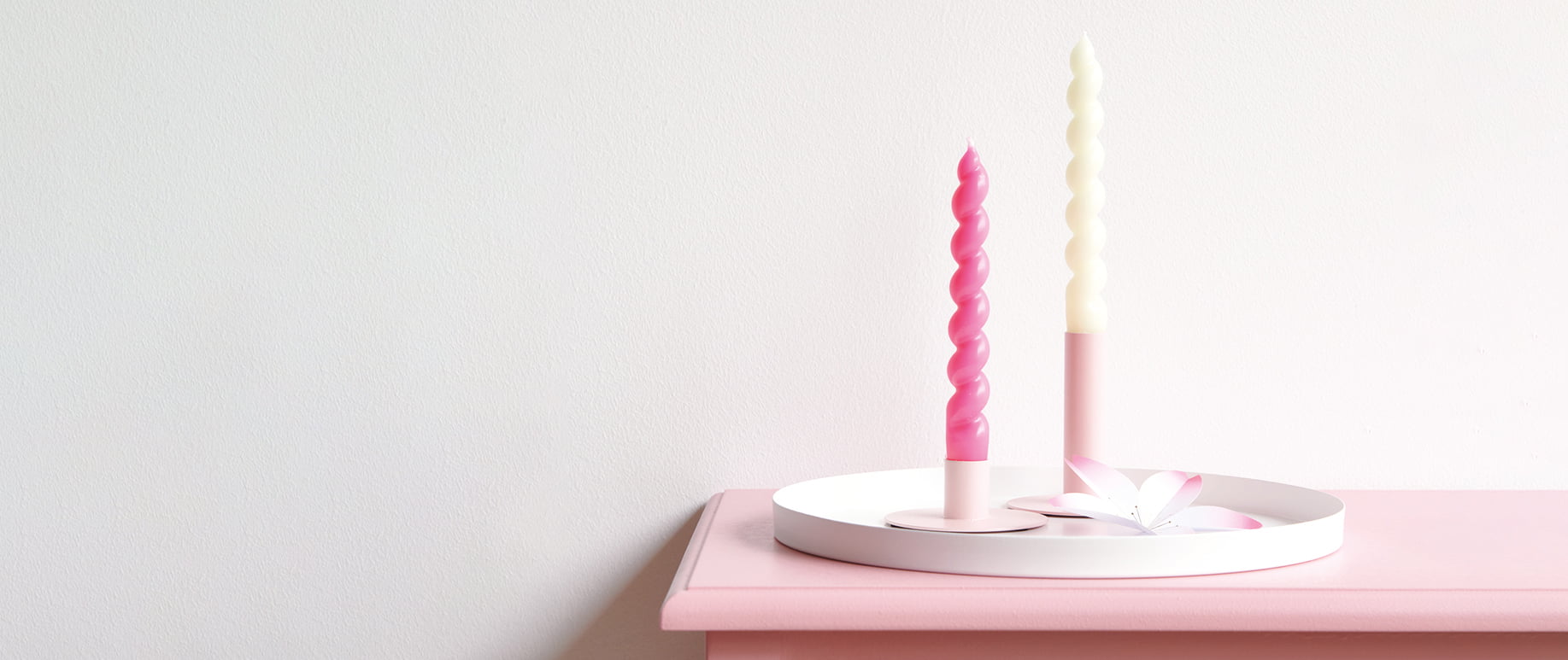 Zwei Kerzenständer sind dekorativ auf einem rosa Regal angerichtet. 