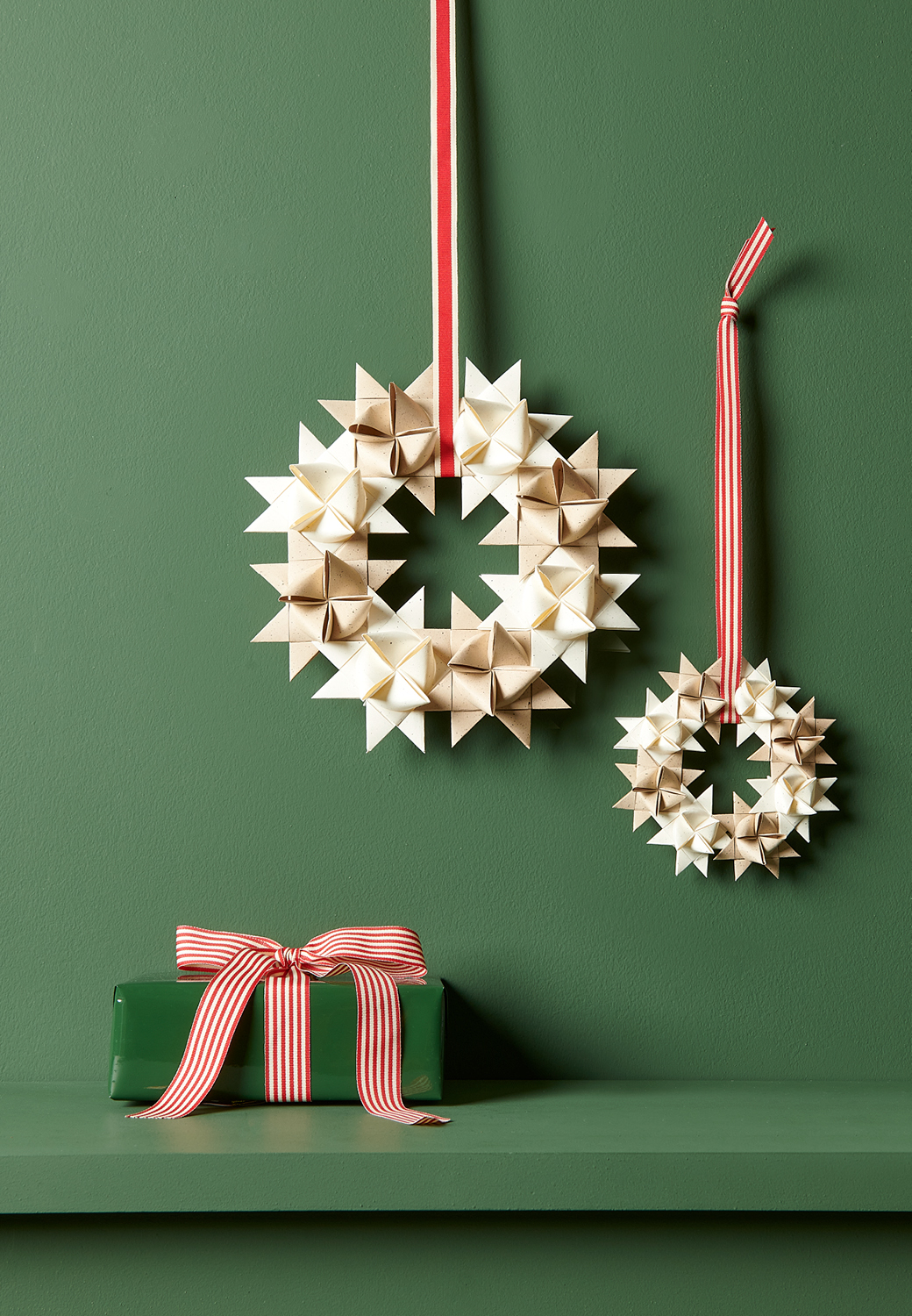 Zwei Kränze aus Fröbelsternen hängen an einer dunkelgrünen Wand