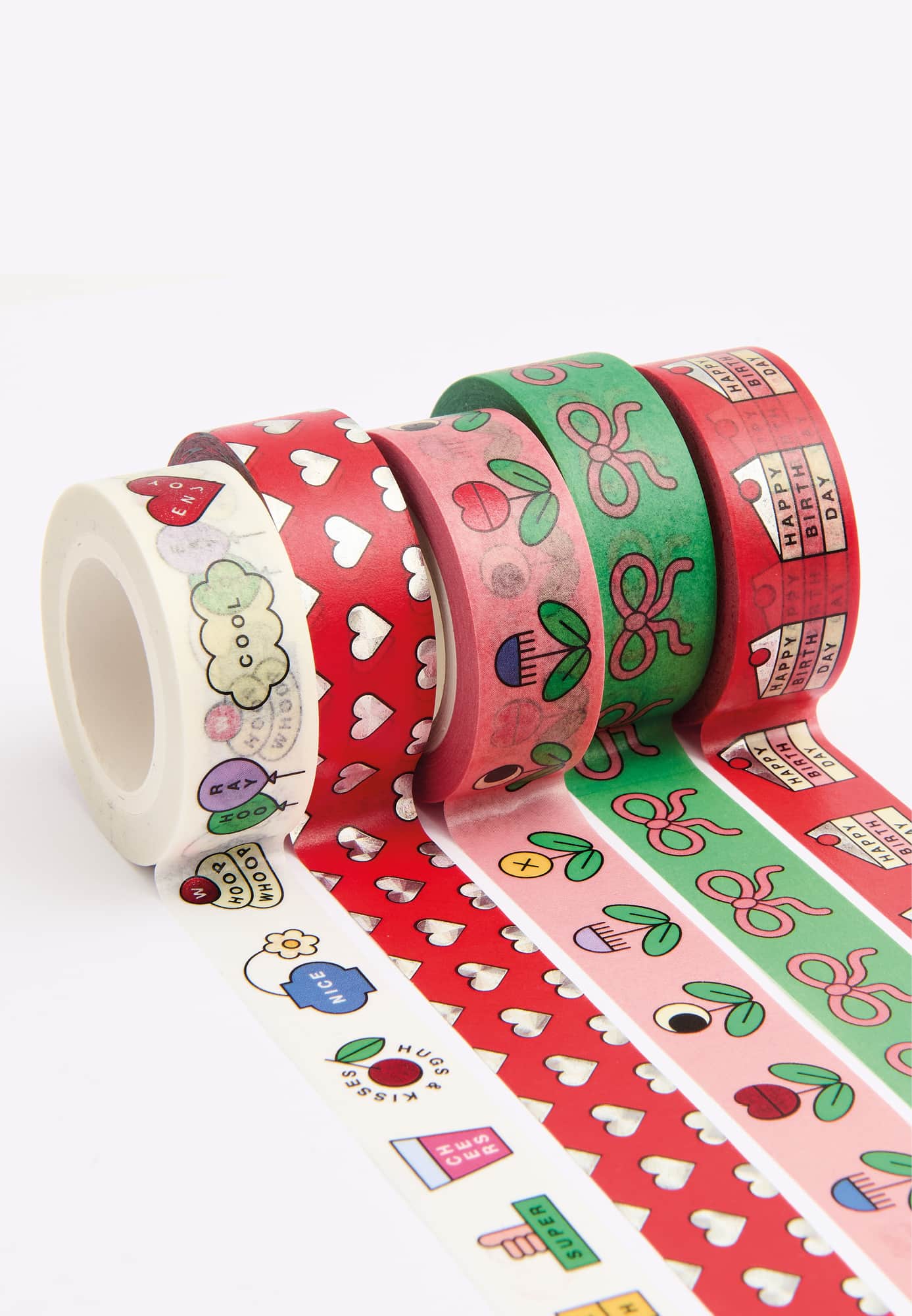 Ausgerollte Washi Tape mit bunten Illustrationen von Herzen, Blumen, Schleifen, Torten und mehr liegen aneinandergereiht auf grauem Hintergrund.
