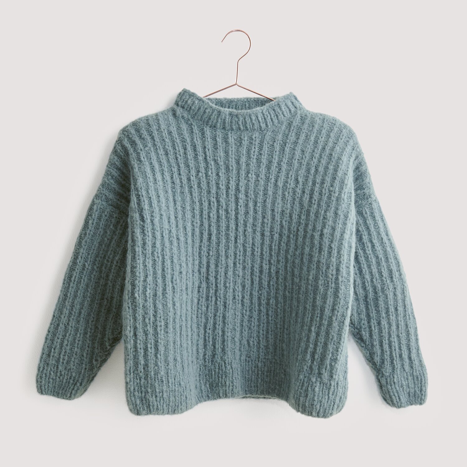 Luxury Knits - Premium Natural Fibres Sprachauswahl deutsch von Rico Design Strickset Pullover Modell 12 aus Luxury Knits, gestrickt in weichem Blau, präsentiert auf einem Kleiderbügel. Ideal für kühle Tage.
