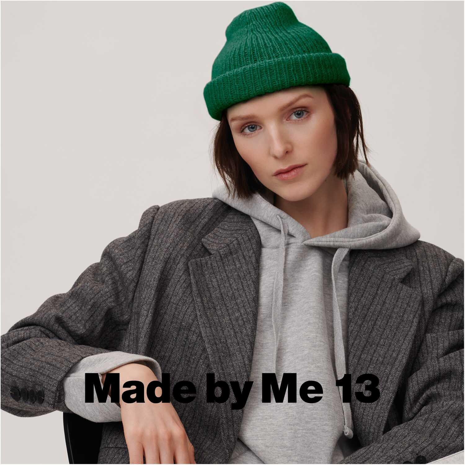 Luxury OMG: Frau in grauem Mantel und grünem Strickmütze von Rico Design, sitzt lässig.