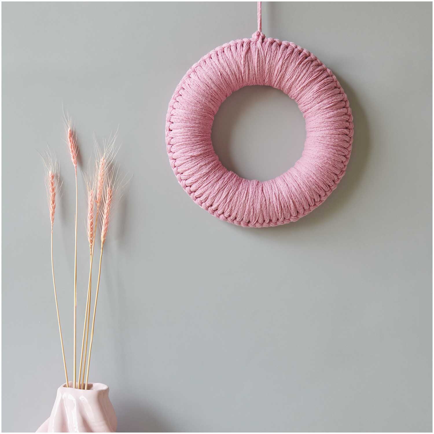 Creative Loopy: Ein rosa Wandkranz aus Wolle von Rico Design, dekorativ neben getrockneten Gräsern.