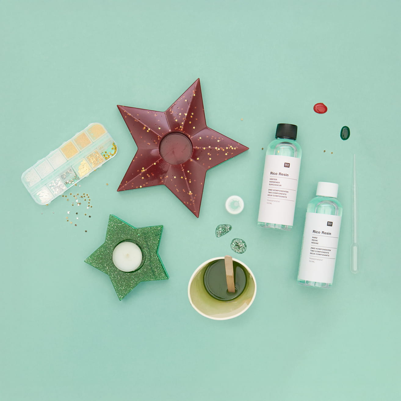 Zwei Teelicht-Halter liegen umgeben von Resin Flaschen und weiterem Zubehör auf grünem Hintergrund.