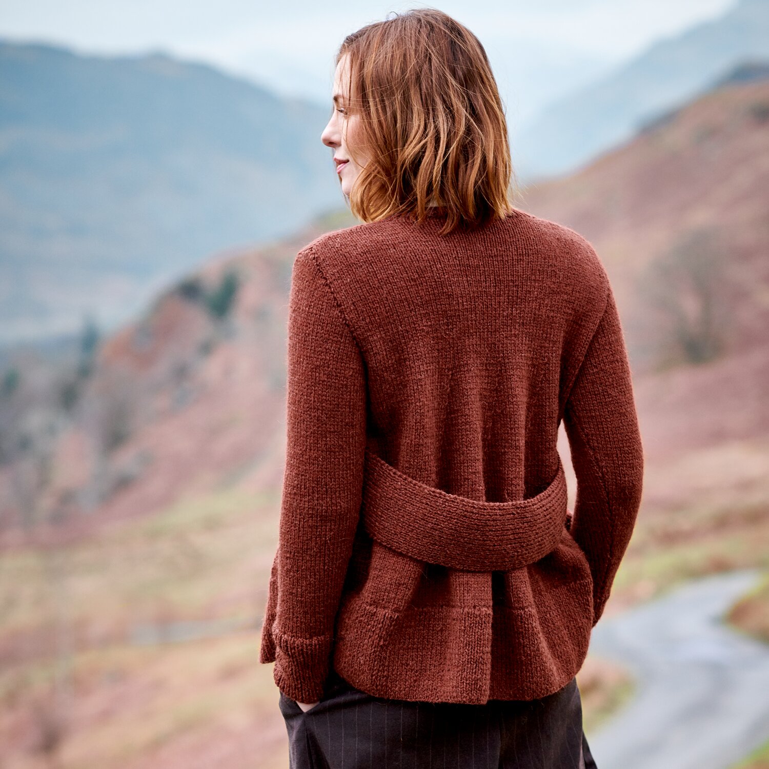 Strickset Pullover Modell 40 aus Lovewool No. 23, hinten getragen von Frau, strukturierter Cardigan mit breitem Bunddetail, stehend in herbstlicher Berglandschaft