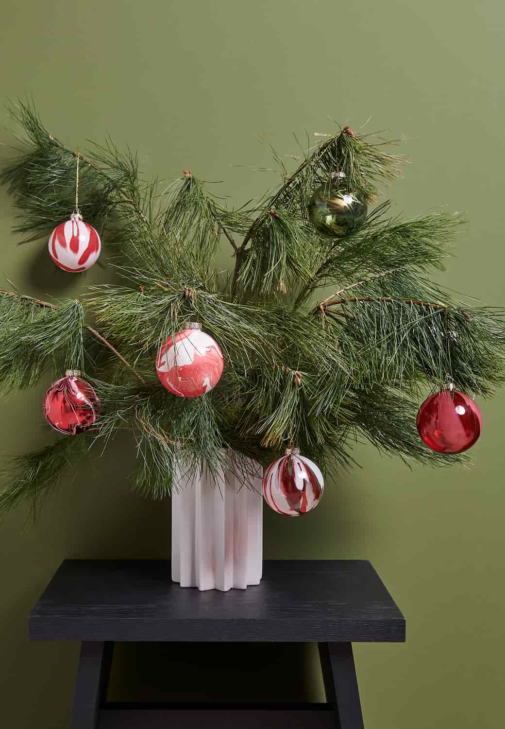 Weihnachtskugeln in Grün und Rot hängen dekorativ an einem Metall-Tannenbaum 