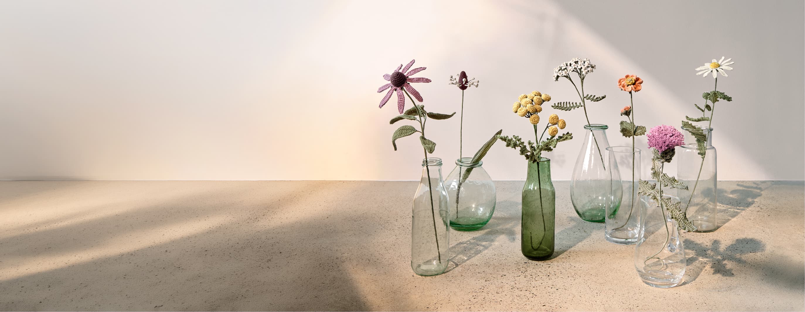 Gehäkelte Wiesenblumen stehen dekorativ in Glasvasen. 