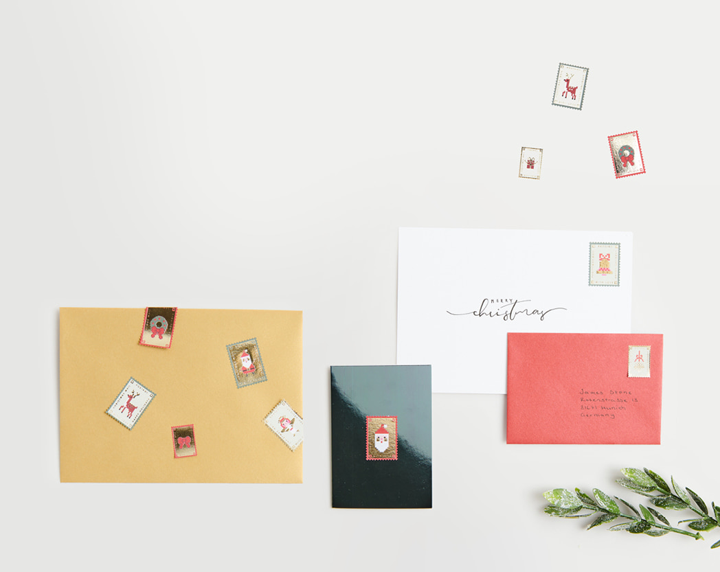 Weihnachtssticker in Form von Briefmarken liegen verteilt und sind dekorativ auf Karten und Umschläge geklebt 