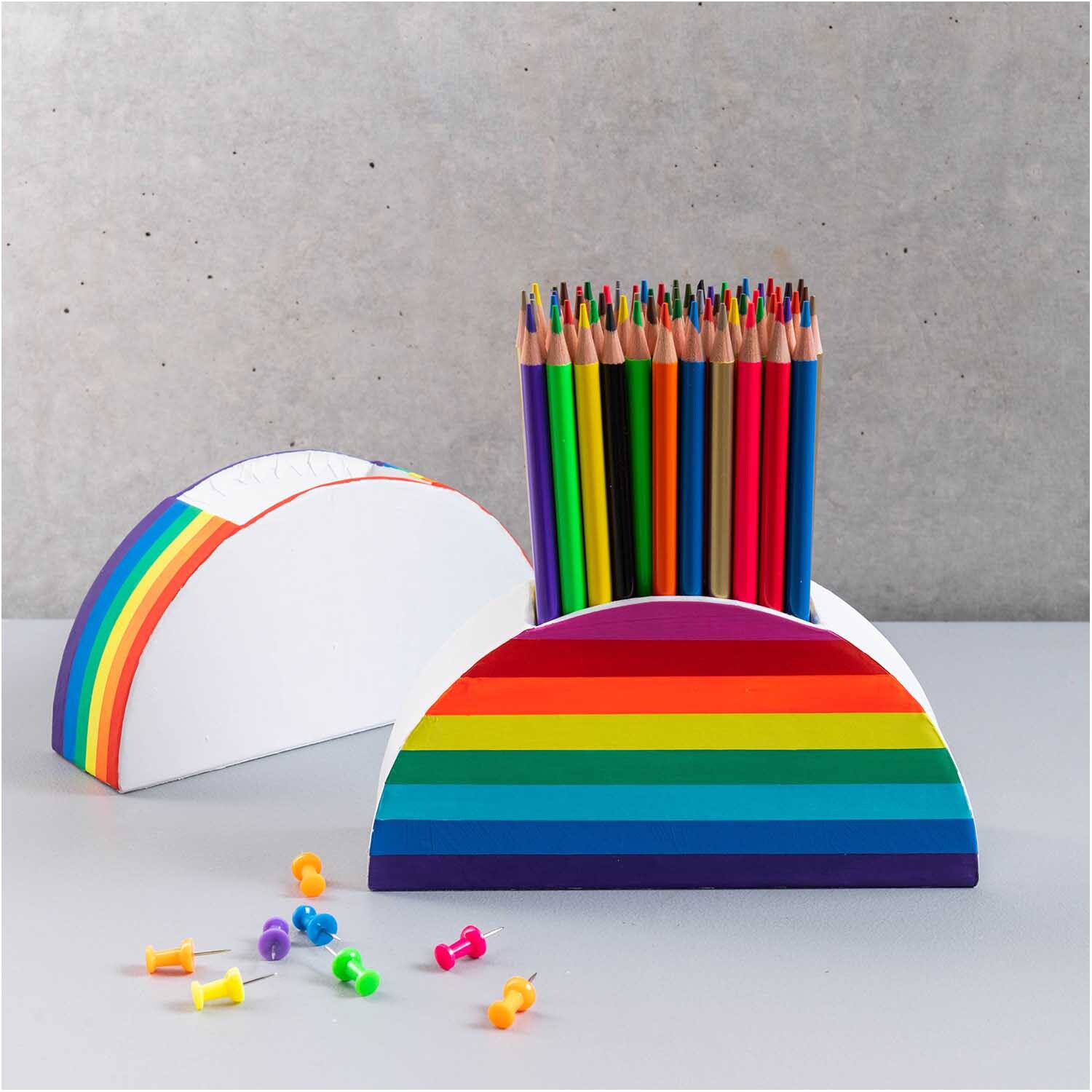 Stiftehalter aus Pappe in halbrunder Form mit Regenbogenstreifen, gefüllt mit bunten Stiften.