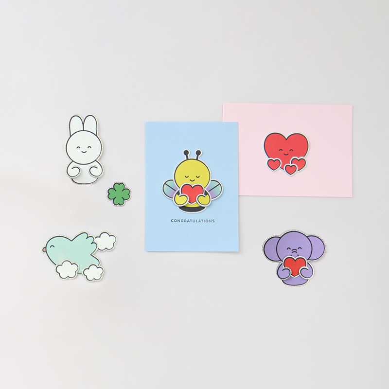 Karten mit Clip-Ons in Form von illustrierten Tieren und Figuren liegen auf gelbem Hintergrund.