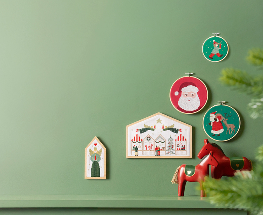 Stickbilder in verschiedenen Größen und mit weihnachtlichen Motiven hängen an einer grünen Wand.