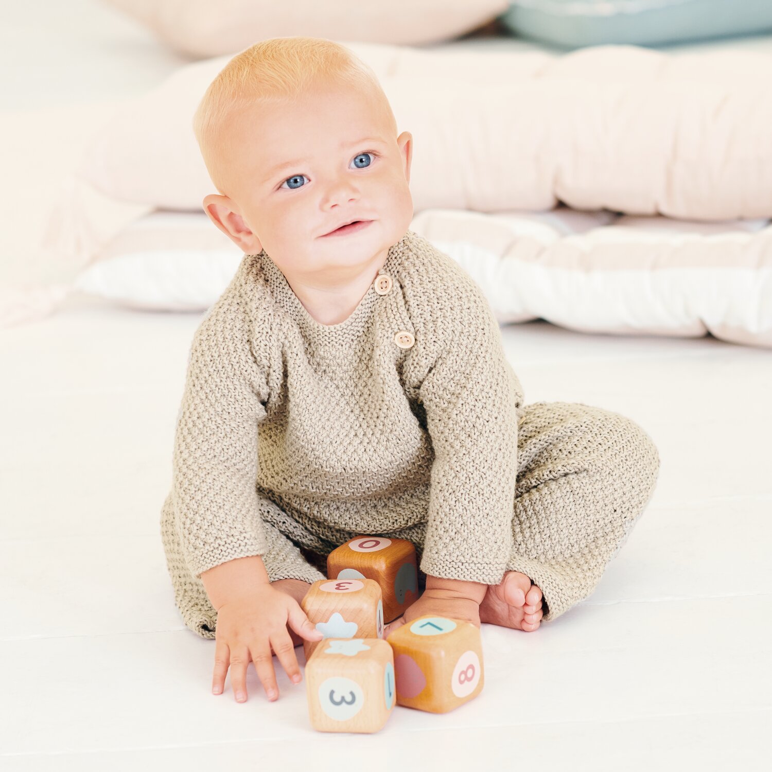Strickset Pullover Modell 06 aus Baby 043: Baby in beigem Strickpullover und Hose spielt mit bunten Würfeln.