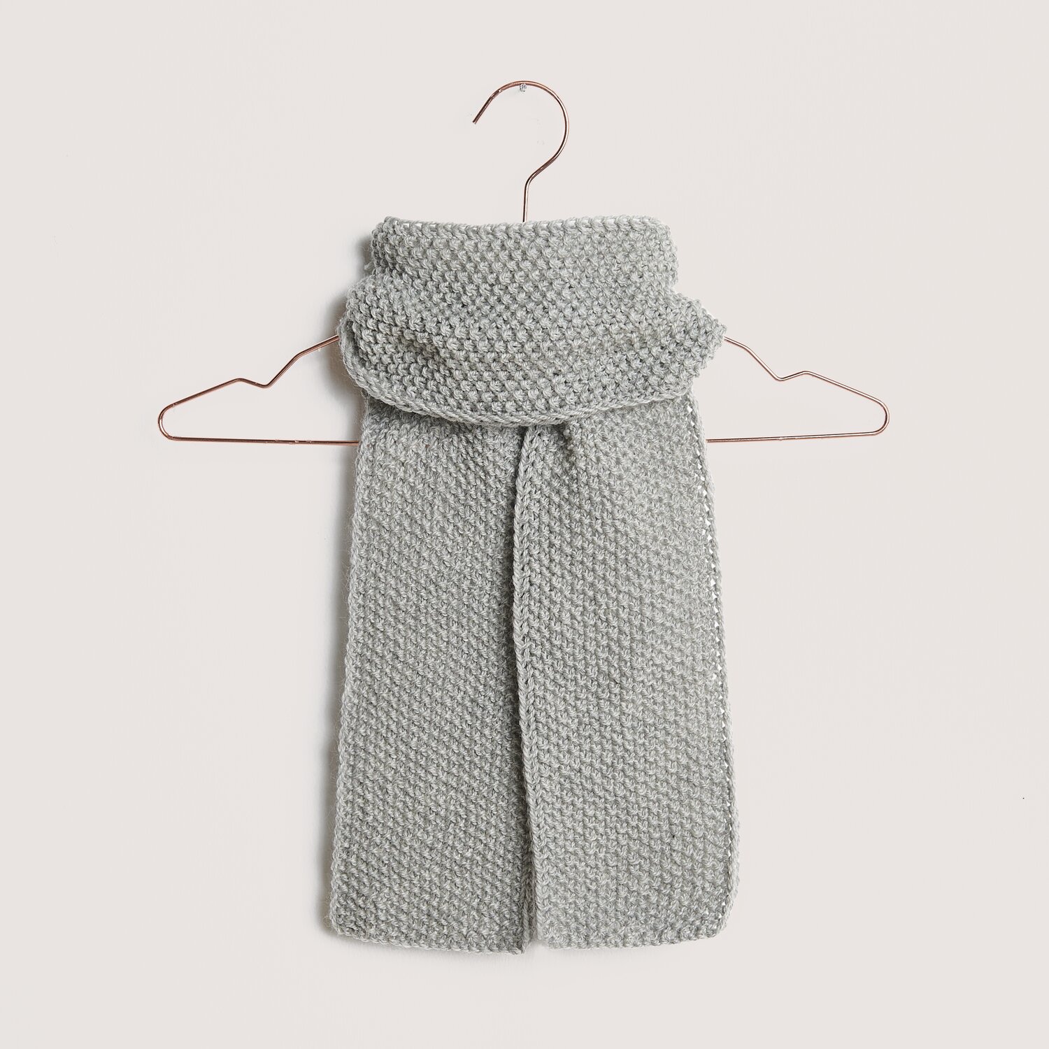 Essentials Soft Merino aran Schal in Hellgrau von Rico Design, gestrickt und auf einem Kleiderbügel präsentiert. Ideal für kalte Tage.