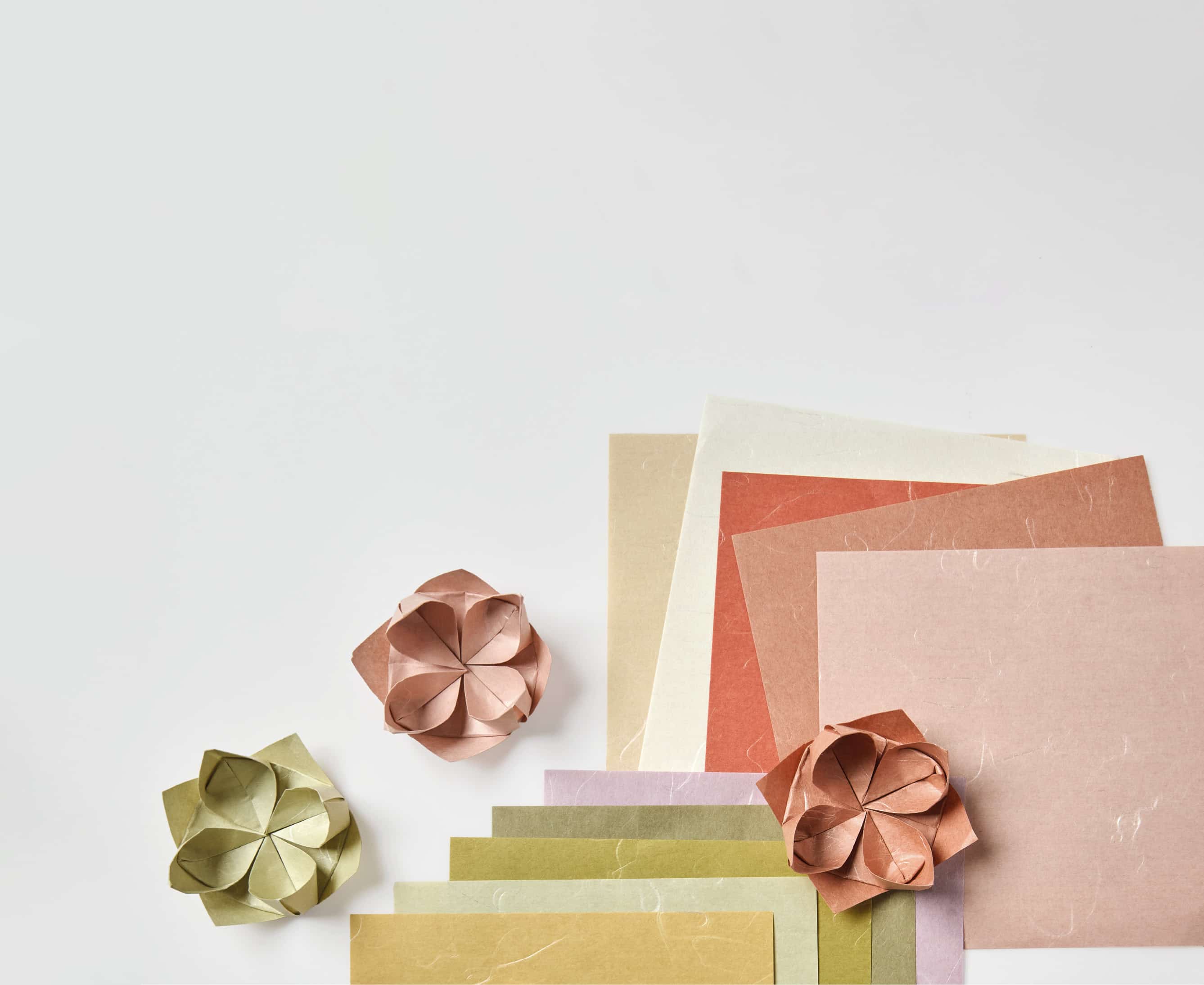 Origamipapier in erdigen Tönen und gefaltete Papierblumen liegen auf grauem Hintergrund. 