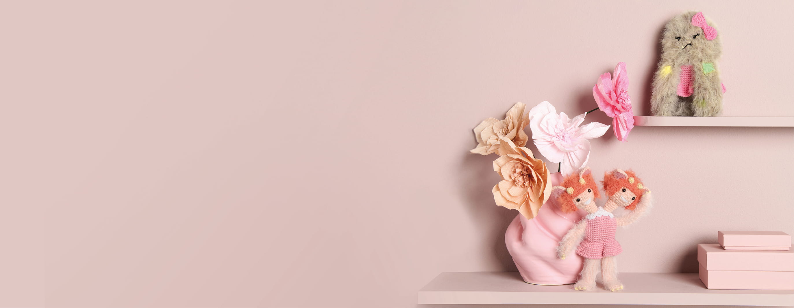 Gehäkelte Monster sind auf Regalbrettern vor einer rosa Wand dekoriert.