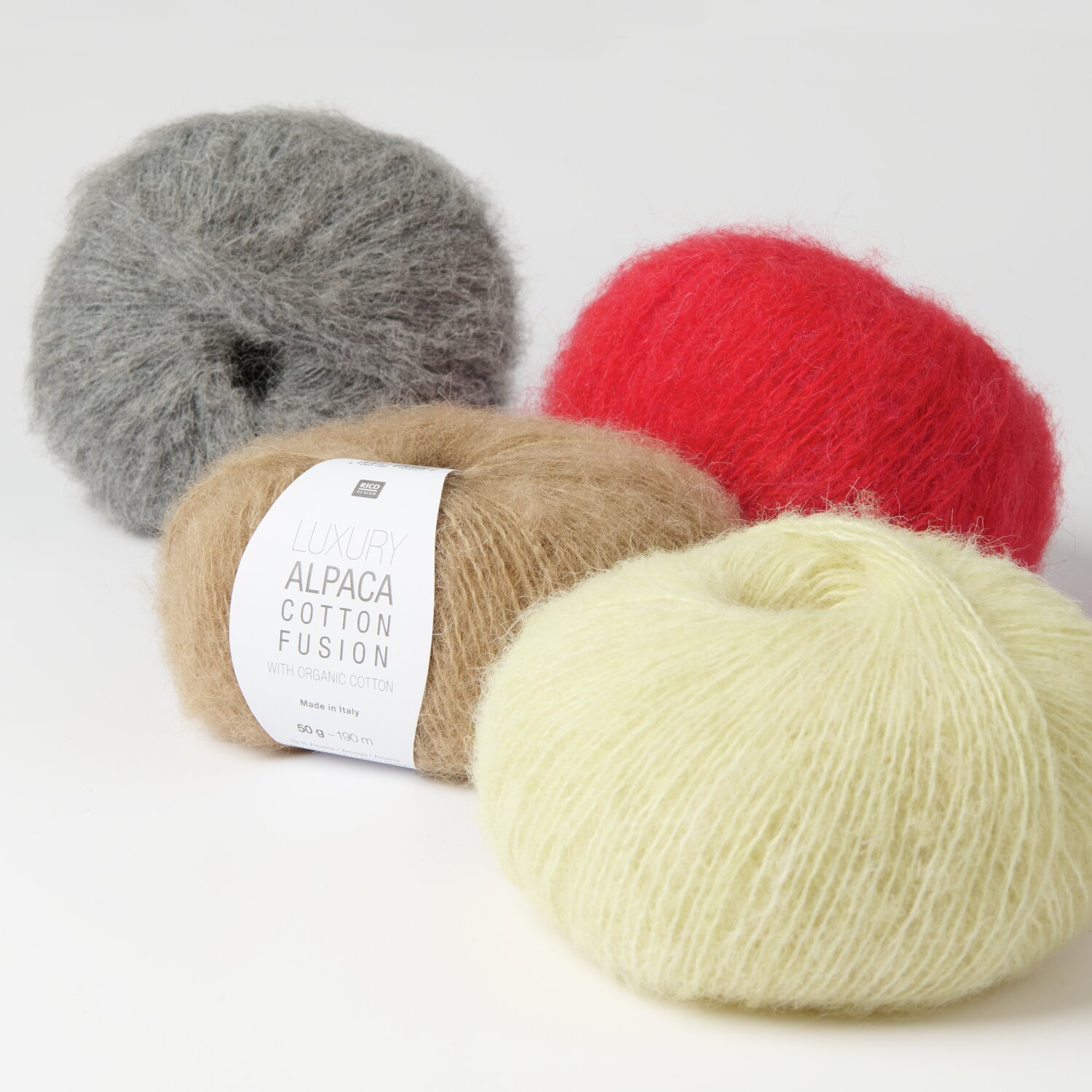 Luxury Alpaca Cotton Fusion: Vier Wollknäuel in Grau, Rot, Beige und Gelb von Rico Design auf weißem Hintergrund.